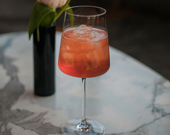 a glass of pink liquid and a black vase with a flower