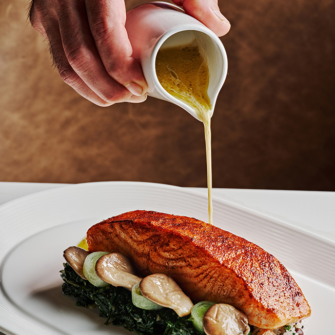 a person pouring sauce on a fish on a plate